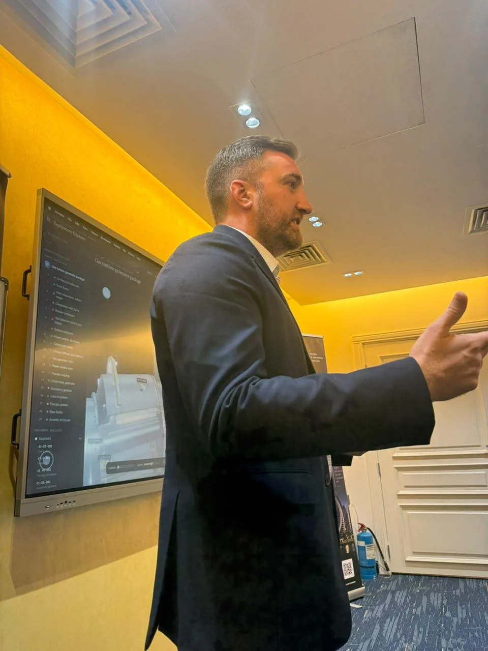 A speaker in a dark blazer presenting to the AI Mavericks audience